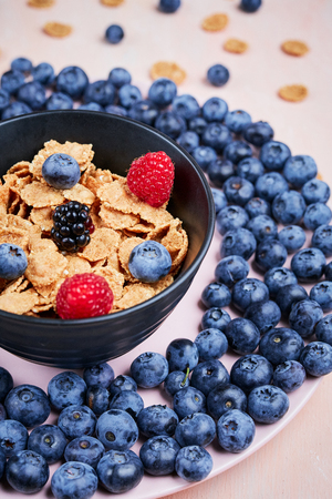 Healthy breakfast bowl with flakes and fresh berries on a plate with blueberries on the pink wooden table.の写真素材