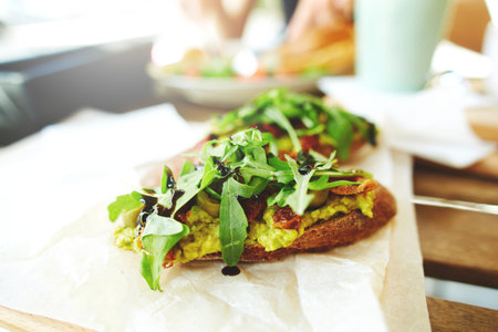 vegan bruschetta with avocado, arugula, dried tomatoes and olives on a wooden table