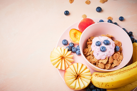 flat lay Food background. Top view of Summer breakfast. berry yoghurt with frefh blueberries, banana and flakes in the pink bowl on the pink wooden table.の写真素材
