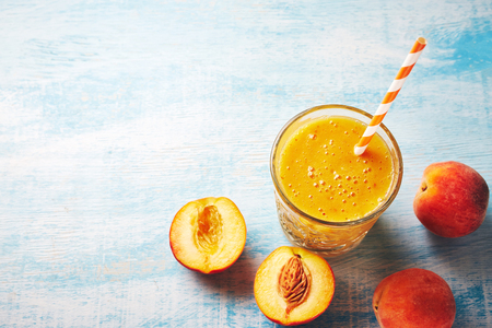 Healthy summer breackfast. Peach smoothies in a glass and halves of ripe peaches on the blue wooden table. Healthy, clean eating, vegan, vegetarian, detox, dieting breakfast food conceptの写真素材