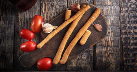 Italian grissini, tomatoes and garlic on the wooden cut board on dark wooden background. top view with copy spaceの写真素材