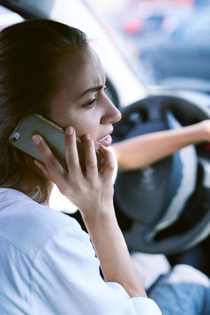 a worried woman sits behind the wheel of a car and calls for help or the insurance companyの写真素材