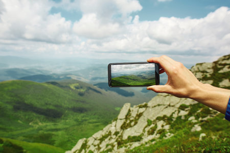 first person view of man photographing mountain landscape by the phone, mans hands with phone on the...
