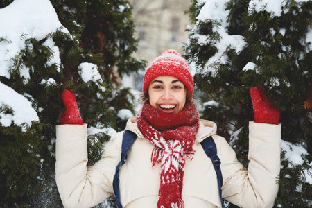 portrait of Cheerful smiling woman in white down jacket and red cap, scarf and mittens on the snowy...