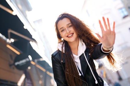 beautiful young woman walking city having fun. joyful Woman in black leather biker jacket and white hoodie laughing and extending hand to the cameraの写真素材