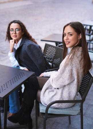 two beautiful stylish women sitting at the table in street cafe at warm spring dayの写真素材