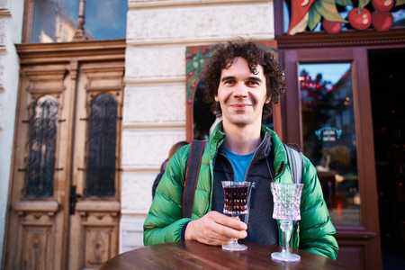 Image of smiling man tourist standing outdoors in city street cafe holding glass drinking wine. Tourist in the old Lviv, Ukraine.の写真素材