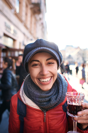Image of laughing young woman standing outdoors in city street cafe holding glass drinking wine. Tourist in the old Lviv, Ukraine.の写真素材