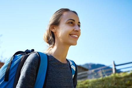 woman hiker with backpack walking outdoors. woman standing on the blue sky background in mountain...