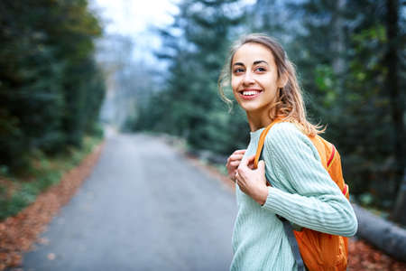 beautiful smiling woman hiker with small backpack standing on the road in the forestの写真素材