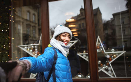 happy smiling woman in winter warm clothes is standing outdoors near the decorated shop windows, holding someone's hand. Follow me conceptの写真素材