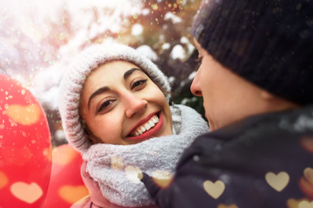 happy hugging couple in warm winter clothes is standing outdoors with a heart shaped red balloons on...