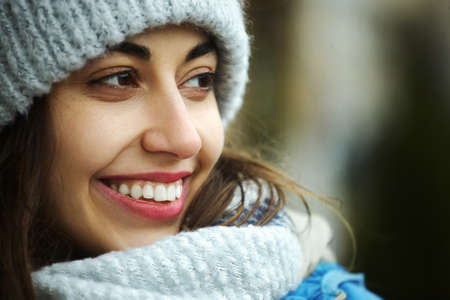 closeup horizontal image of a side looking happy smiling woman in warm winter clothes against the background of bright Christmas lightsの写真素材