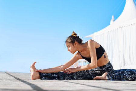 Photo of young sports woman make yoga exercises on seaside. Side view of athletic lady doing...