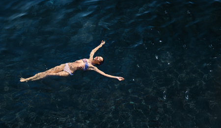 aerial view of a beautiful sexy slim woman floating and reraxing in the deep blue sea. relaxed woman floating on transparent turquoise sea. Summer seascape with girl and azure waterの写真素材
