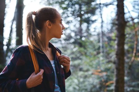 Portrait of a woman hiker walking on the trail in the woods. Beautiful happy stylish traveling girl with backpack on a forest background.の写真素材