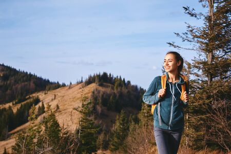 Portrait of a happy woman hiker standing on the slope of mountain ridge against mountains, blue cloudy sky on background. The woman is happy and looking at camera. Travel and active lifestyle concept.の写真素材