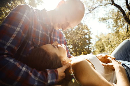 Young romantic couple in love spend time in the park. Young woman lying on knees of man and looking at each other with sun rays background. Happy moments together. Dating and romantic relationship concept.の写真素材