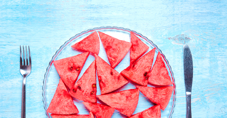 Watermelon slices without skin on the transparent glass plate on blue wooden table. Top view, flat lay. Summertime conceptの写真素材