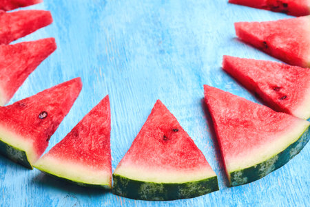 Triangular ripe watermelon slices on blue wooden table spread out by a ring in the form of a shark...