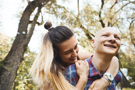 Close up image of young couple having fun and laughing in park at summer day. Boyfriend carrying his girlfriend on back. Happy moments together. Love, relationship, family and people concept.の写真素材
