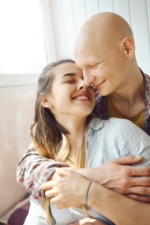 Affectionate young man with bald head embracing young woman from behind. young enamoured couple spending time together at home, people show happiness, tender feelings for each other. love, relationship, family and people concept.の写真素材
