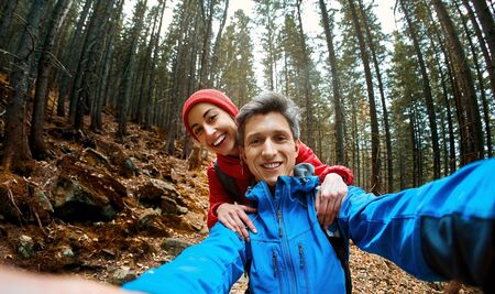 smiling happy couple hikers with backpacks making selfie on the dark dramatic mossy woods background while hiking in mountains in Western Ukraine.の写真素材