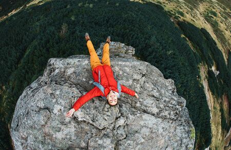 top view of woman hiker in red jacket lying on the cliff in mountains with raised handsの写真素材