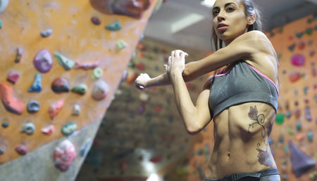 Athletic woman with muscular naked torso doing stretching before climb in indoor climbing gym. Exercising and training in climbing gym. Concept of strength, sport, healthy lifestyle.の写真素材