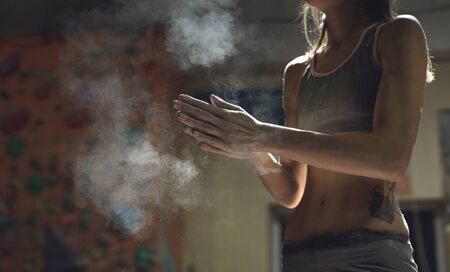 closeup view of woman climber is chalking and clapping hands with white chalk powder before climb in indoor climbing gym. woman getting ready to climbing. exercising and training in climbing gym.の写真素材