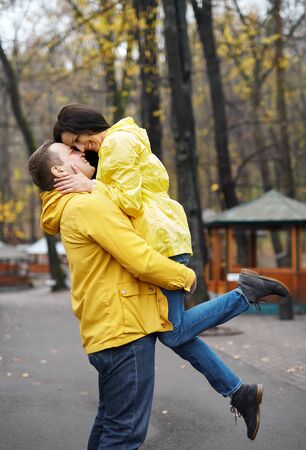 couple in yellow jackets embracing and kissing, walking in the autumn park. Happy young family spends time together. Love and good relationship concept. Autumn concept.の写真素材
