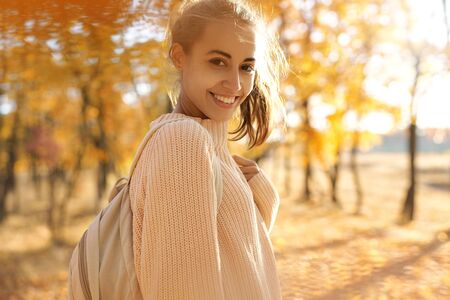Autumn outdoor portrait of young smiling woman in autumn park with colorful leaves on fall nature background. Pretty stylish smiling woman walking, in good mood. Outdoor bright lifestyle portrait. Season and people concept.の写真素材