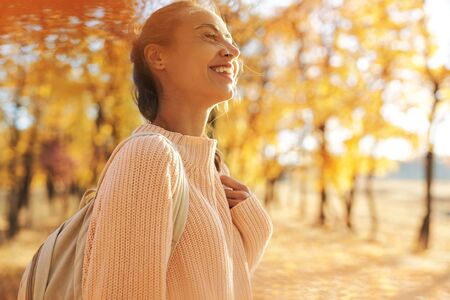 Autumn outdoor portrait of young smiling woman in autumn park with colorful leaves on fall nature background. Pretty stylish smiling woman walking, in good mood. Outdoor bright lifestyle portrait. Season and people concept.の写真素材