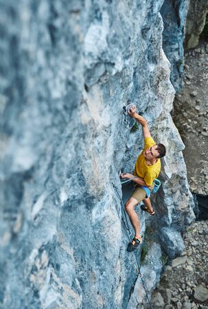 top view of man rock climber in yellow t-shirt, climbing on a cliff, searching, reaching and gripping hold, attaching rope. outdoors rock climbing and active lifestyle concept, 4K stock footageの写真素材