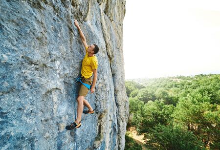 Young strong man climbing challenging route on a high vertical limestone cliff, resting and considers route. Conquering, overcoming and active lifestyle concept.の写真素材