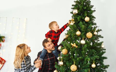 Young family decorating Christmas tree on the eve of holiday. Young parents and their little son enjoying their winter holidays together at home. Merry Christmas and Happy New Year.の写真素材