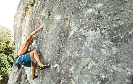 strong muscular man rock climber with naked torso dynamically climbing on a vertical cliff, making hard wide move and gripping hold.の写真素材