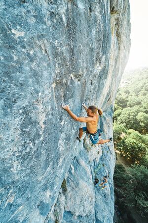strong muscular man rock climber with naked torso dynamically climbing on a vertical cliff, making hard wide move and gripping hold.の写真素材