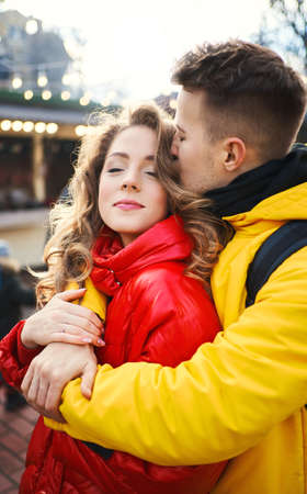 young man in yellow down jacket embracing his girlfriend, spending time together in the city, having a date. urban romantic portrait. Romantic, love and Valentine's Day concept.の写真素材