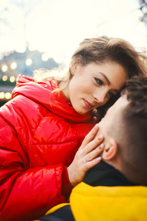 lovely young woman in red down jacket embracing, touches face of boyfriend, spending time together in the city, having a date. urban romantic portrait. Romantic, love and Valentine's Day concept.の写真素材