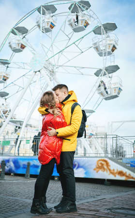 young romantic couple kissing, hugging, walking on the street, wearning in bright down jackets. spending time together, having a date, ferris wheel on background. Romantic, love and Valentine's Day concept.の写真素材