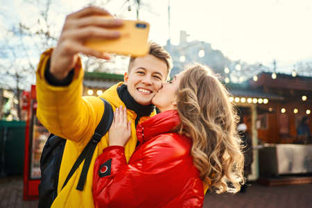 young romantic couple in love making selfie on smartphone, smile to to the camera, woman kissing in cheek her boyfriend. Spending time together in the city, having a date. urban romantic portrait. Romantic, love and Valentine's Day concept.の写真素材