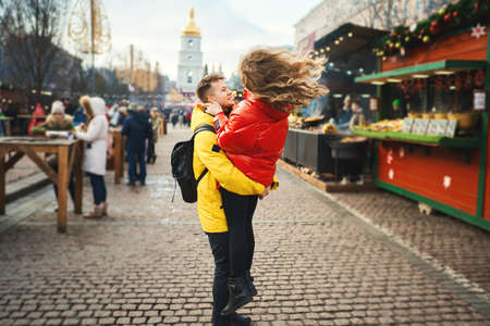 Young emotional couple having fun together and looking happy, handsome young man carrying his girlfriend while walking on the street. spending time together, having a date. urban background. Romantic, love and Valentine's Day concept.の写真素材