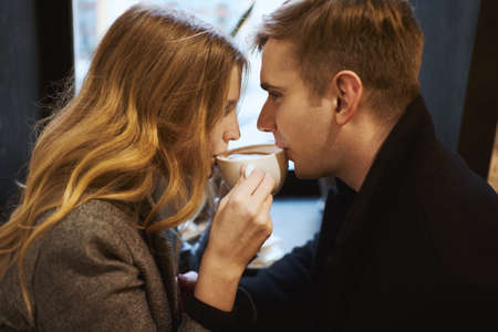 young happy couple sitting over the window in cafe and drinking coffee from one cup. happy moments together. having a date. Romantic, love and Valentine's Day concept.の写真素材