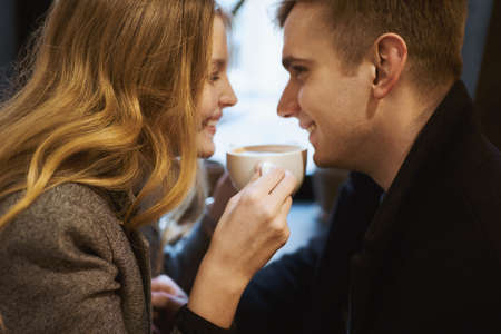 closeup portrait of young happy couple sitting over the window in cafe, smilling, laughing and drinking coffee. happy moments together. having a date. Romantic, love and Valentine's Day concept.の写真素材