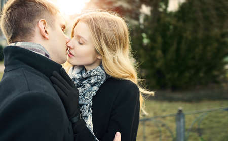 portrait of attractive blonde woman in black coat kissing her boyfriend with closed eyes, feeling comfortable together, happy moments together. Romantic, love and Valentine's Day concept.の写真素材