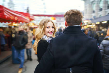 elegant romantic couple walking city street in a crowd of people. attractive blonde woman in black coat turn around and looking at camera. lifestyle portrait. Romantic, love and Valentine's Day concept.の写真素材
