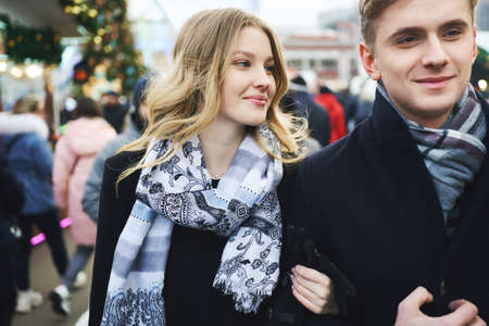 young beautiful blonde couple walking city street in a crowd of people. boyfriend and girlfriend enjoying a date, wearing in black coats. urban romantic portrait. Romantic, love and Valentine's Day concept.の写真素材