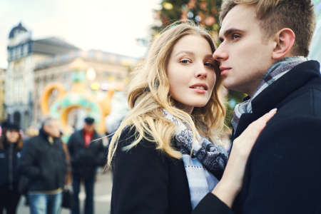 closeup portrait of attractive blonde woman in black coat embracing her boyfriend and looking to camera, feeling comfortable together, close to each other, happy moments together. Romantic, love and Valentine's Day concept.