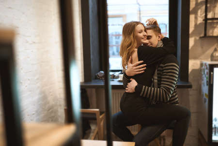 romantic happy couple sitting over the window in cafe and hugging each other. portrait of attractive blonde woman and man having a date. happy moments together. Romantic, love and Valentine's Day concept.の写真素材